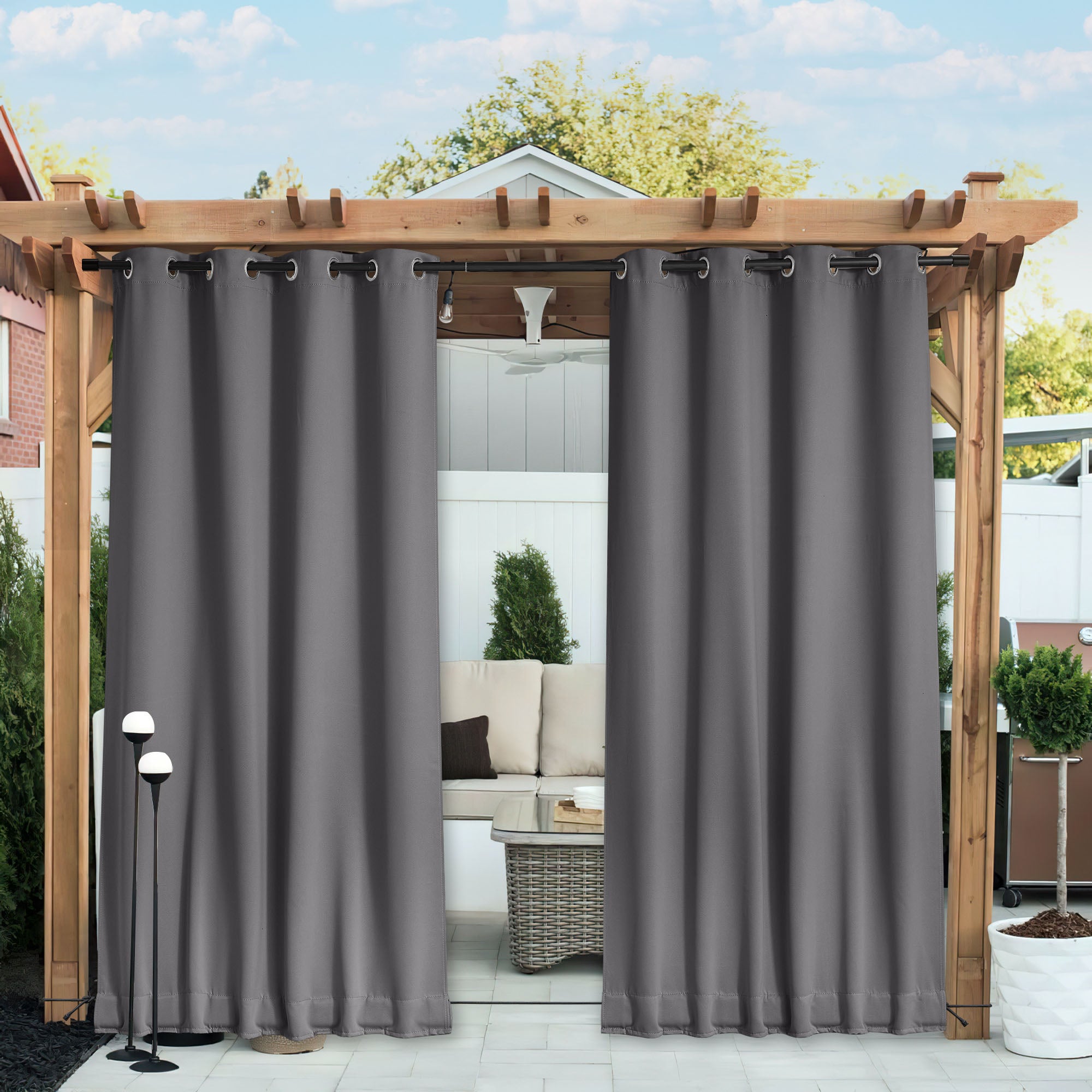 Two charcoal grey waterproof blackout outdoor curtains with grommets hanging from a pergola, providing patio privacy.