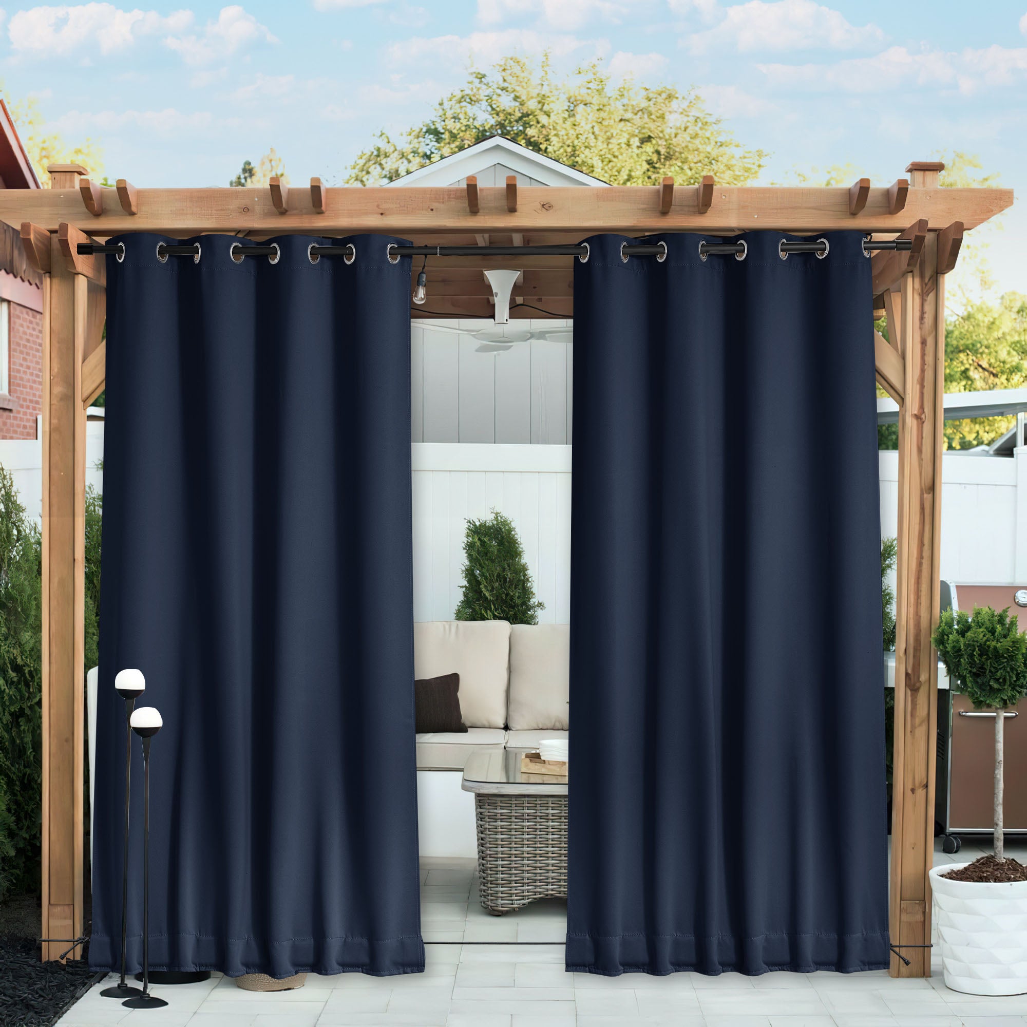 Navy blue waterproof blackout outdoor curtains with grommets, partially open on a wooden pergola, showing a patio lounge.