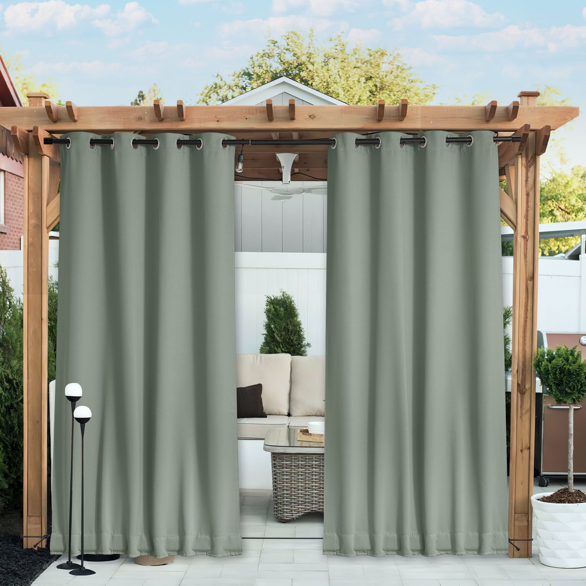 Sage green waterproof blackout outdoor curtains on a wooden pergola, partially open to an outdoor patio with sofa.