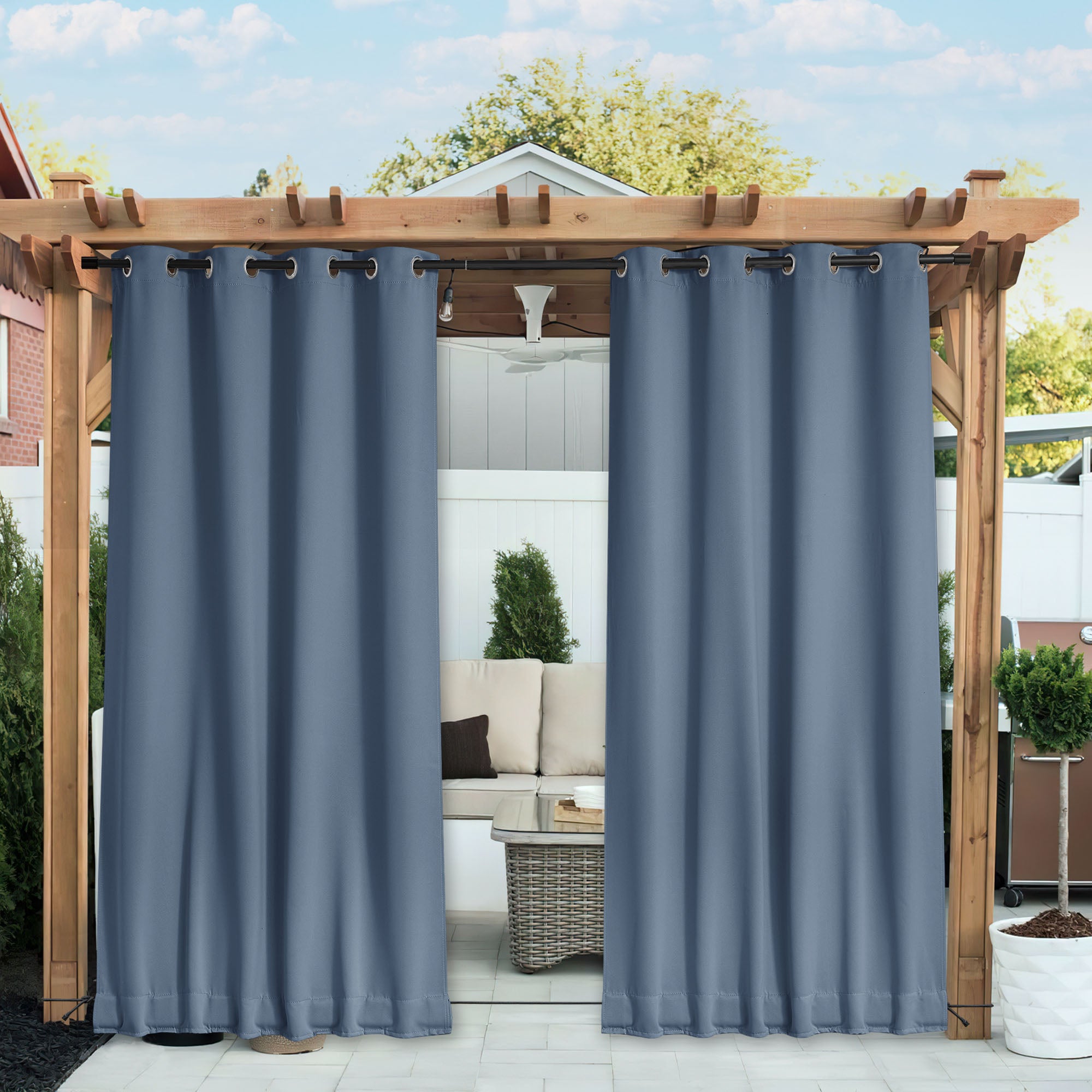 Two blue waterproof blackout outdoor curtains hang from a pergola, slightly open to show a patio seating area with a couch.