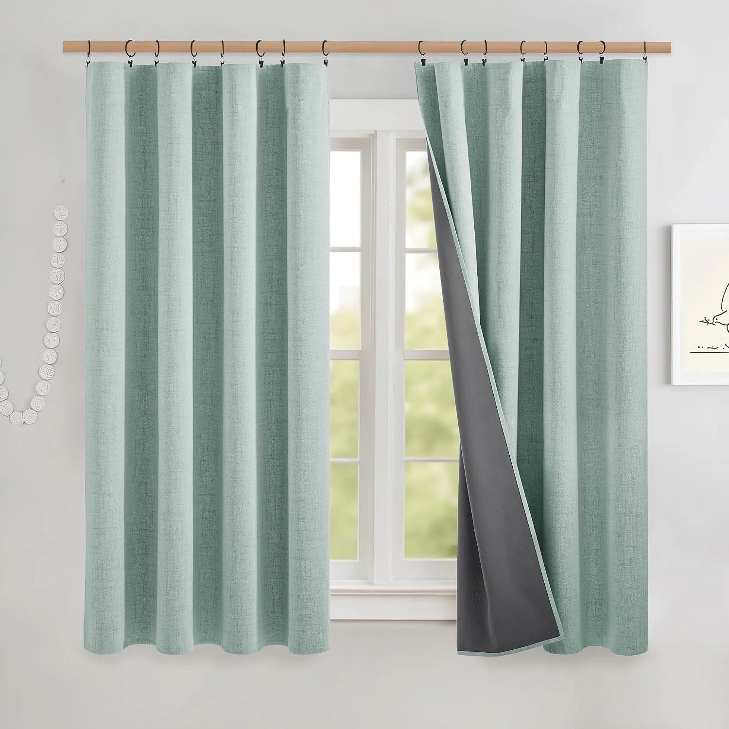 Light aqua textured blackout curtains with black ring hooks on a wooden rod