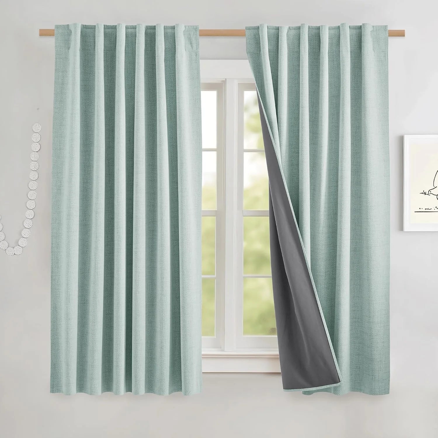 Light aqua textured blackout curtains on a wooden rod, one panel pulled back to show gray lining