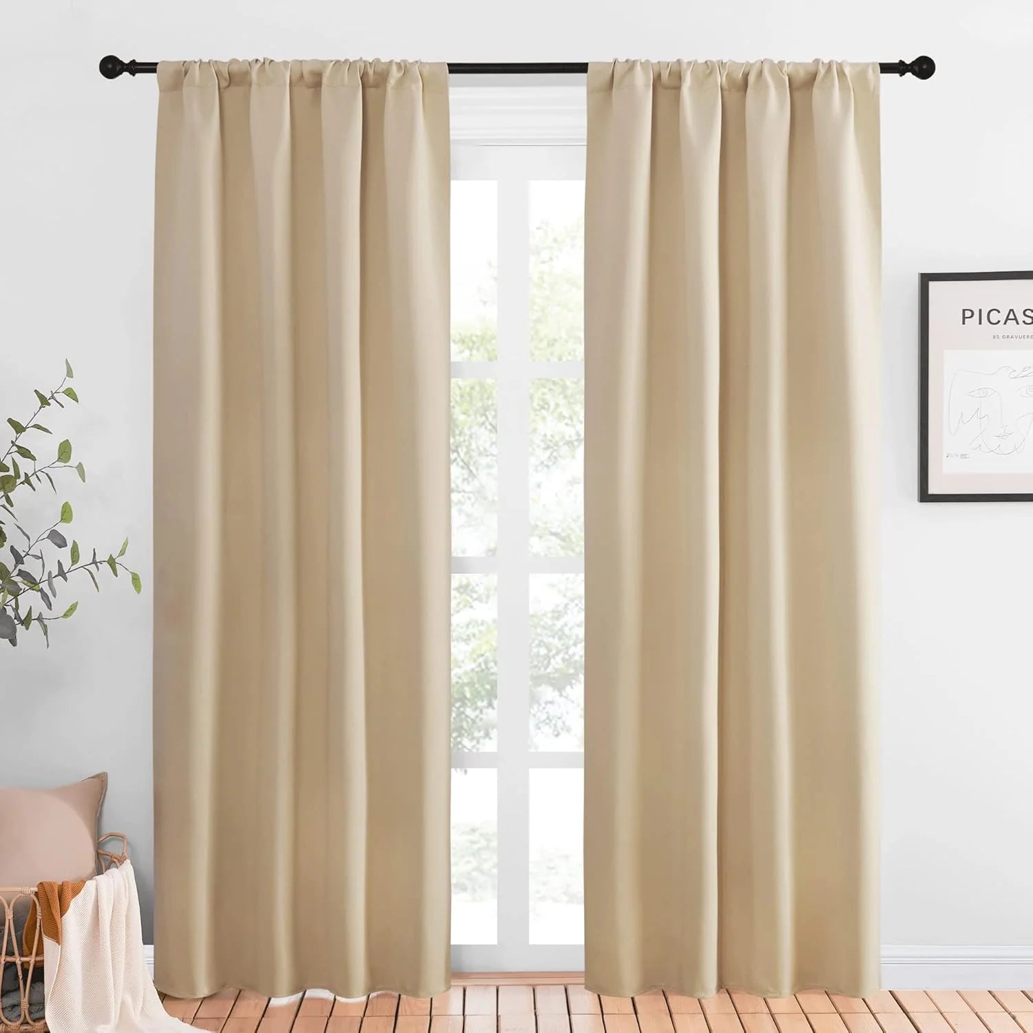 Beige rod pocket blackout curtains hanging on a black curtain rod by a bright window