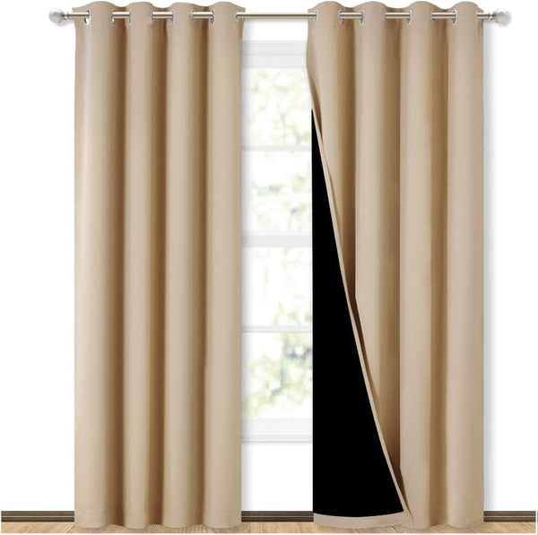 Beige blackout curtains with silver grommet tops hanging on a rod, one panel showing its black lining.