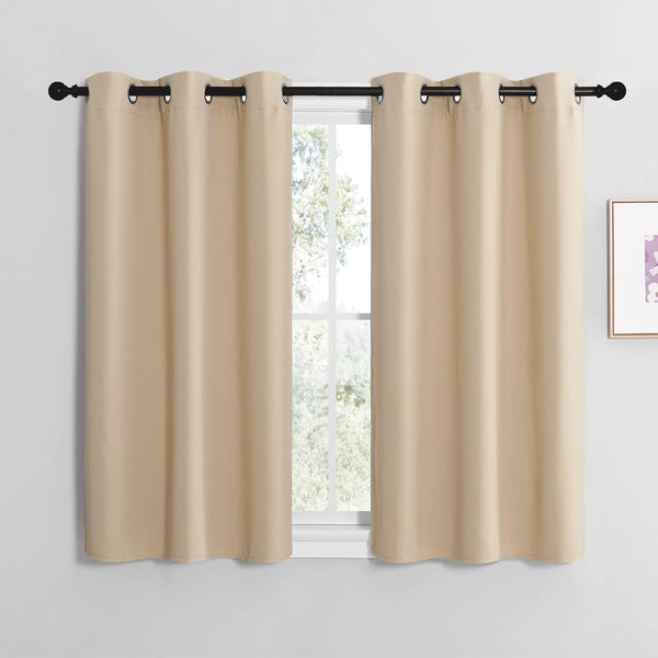 Pair of short beige blackout curtains with silver grommet tops on a black rod over a window.