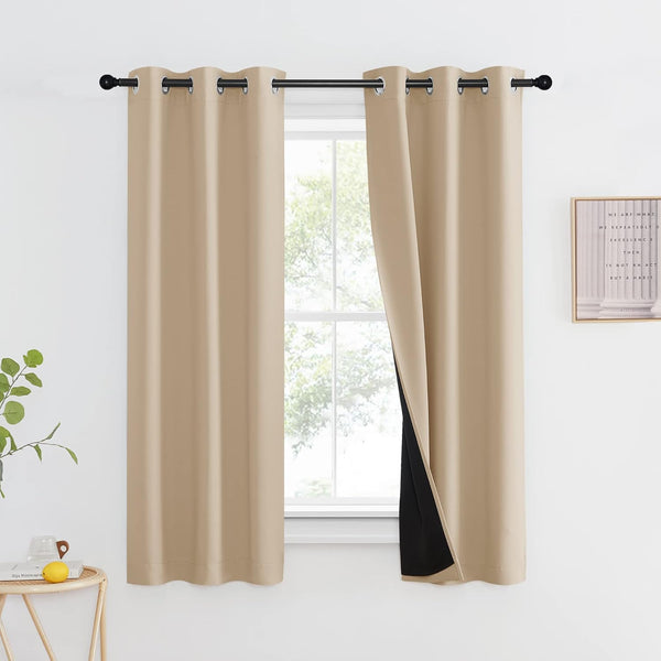 Beige grommet top blackout curtains with visible black thermal lining hanging on a black rod.