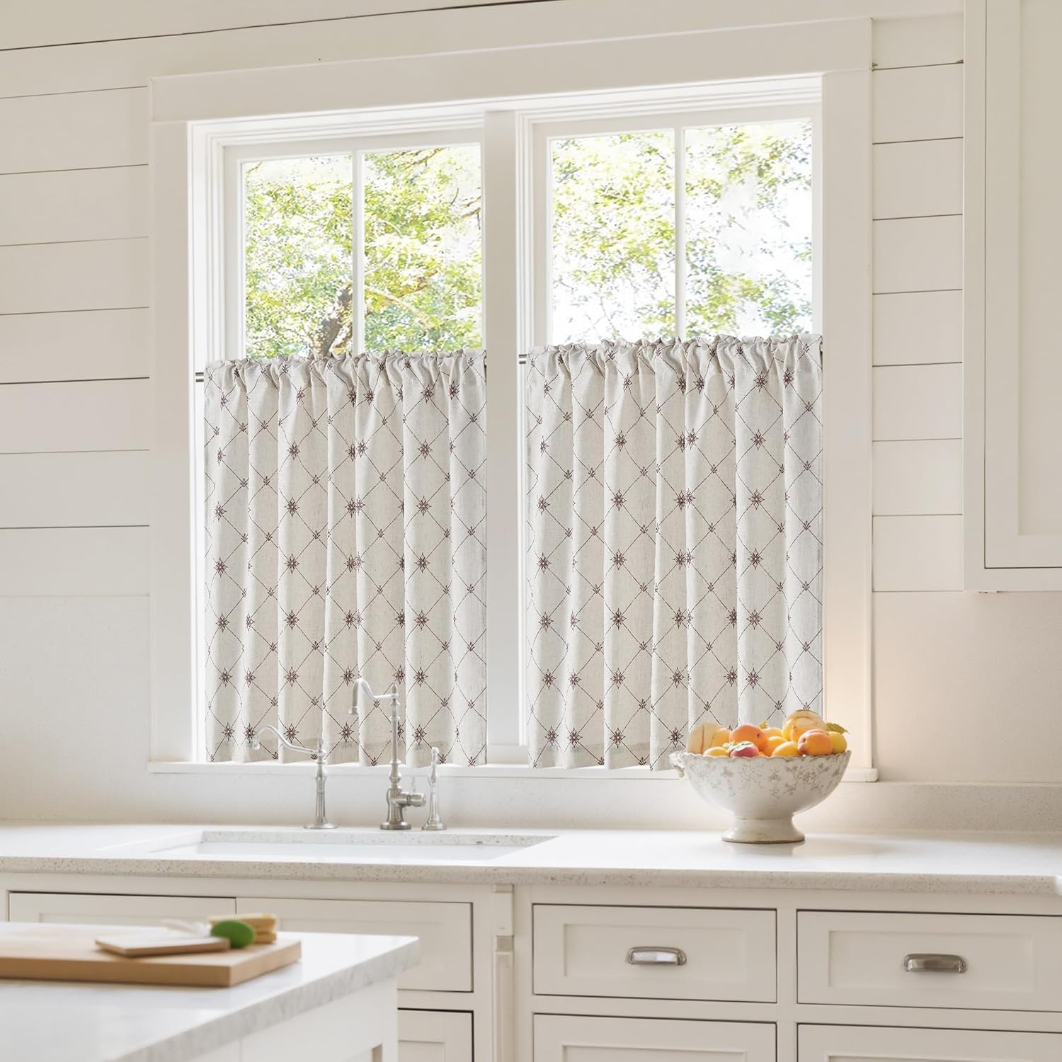 Beige gathered cafe curtains with dark embroidered diamond pattern in a kitchen window.