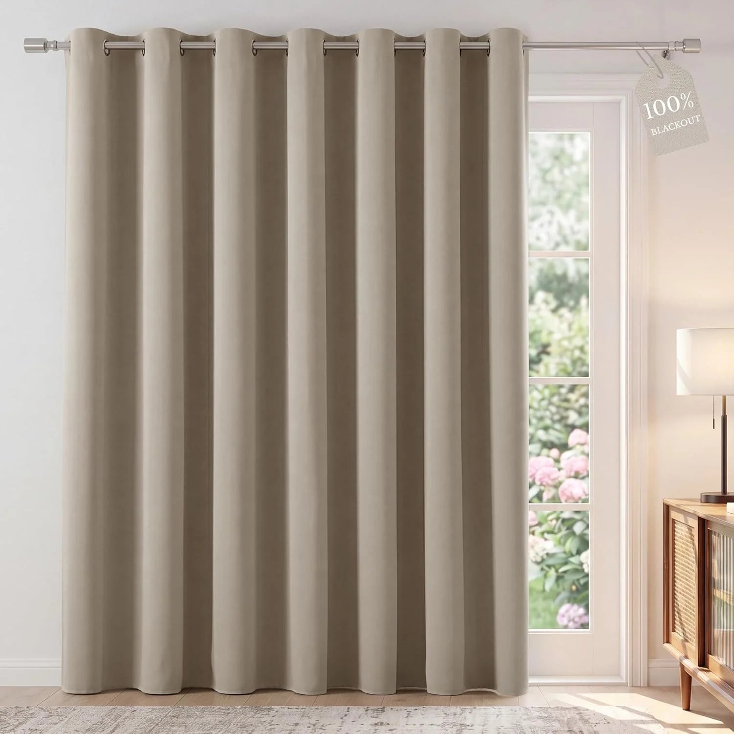 Neutral beige grommet top blackout curtain panel covering a patio door with garden view.