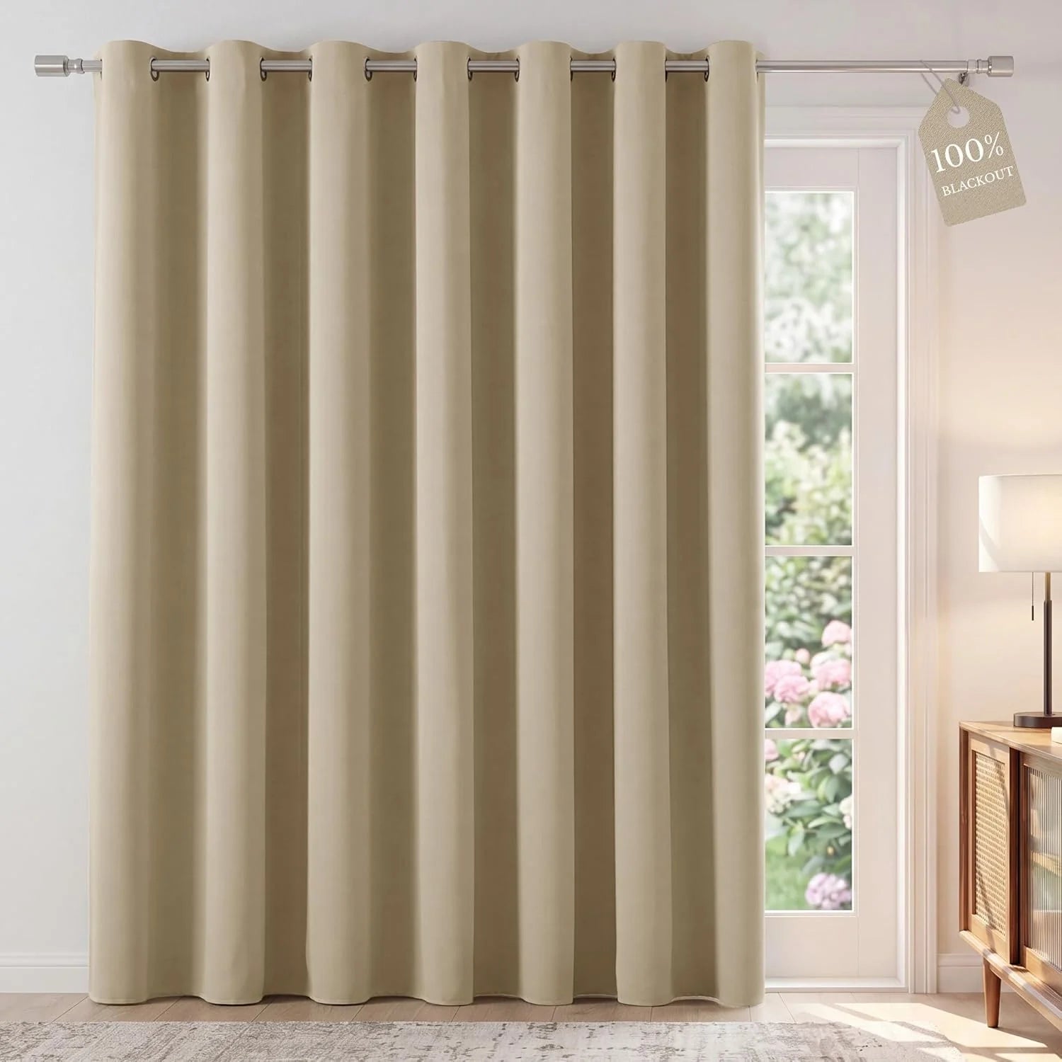Beige grommet top blackout curtain panel covering a patio door, 100% blackout tag visible.