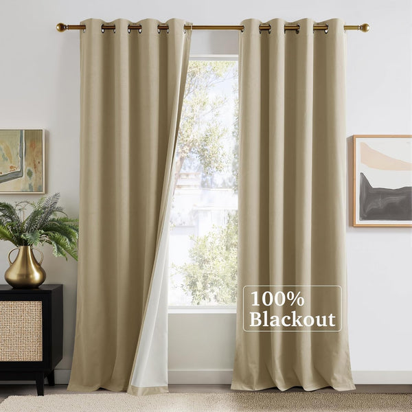 Pair of beige grommet 100% blackout curtains on a gold rod, one panel open to a window.