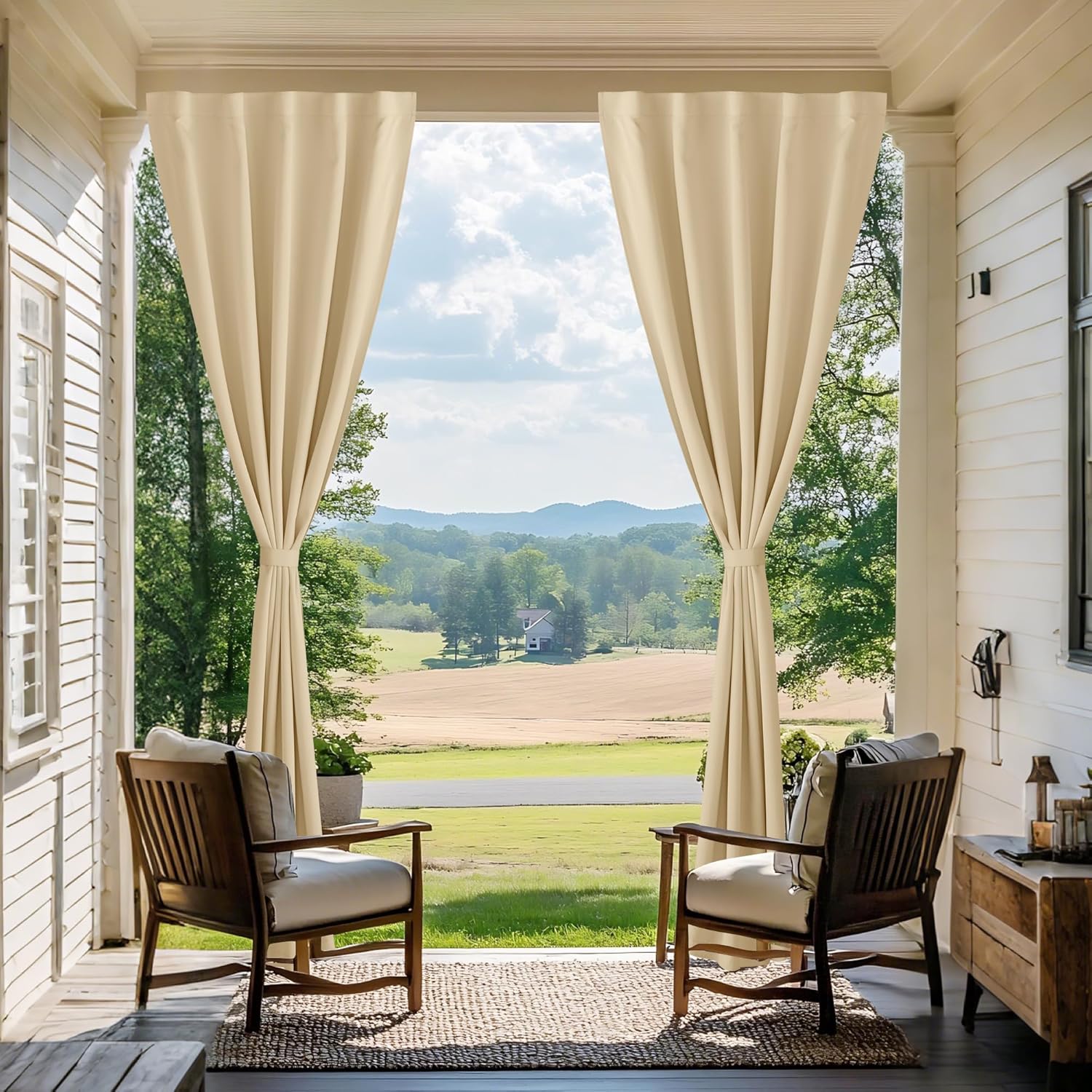 Light beige grommet outdoor curtains tied back on a porch, framing a scenic countryside view.