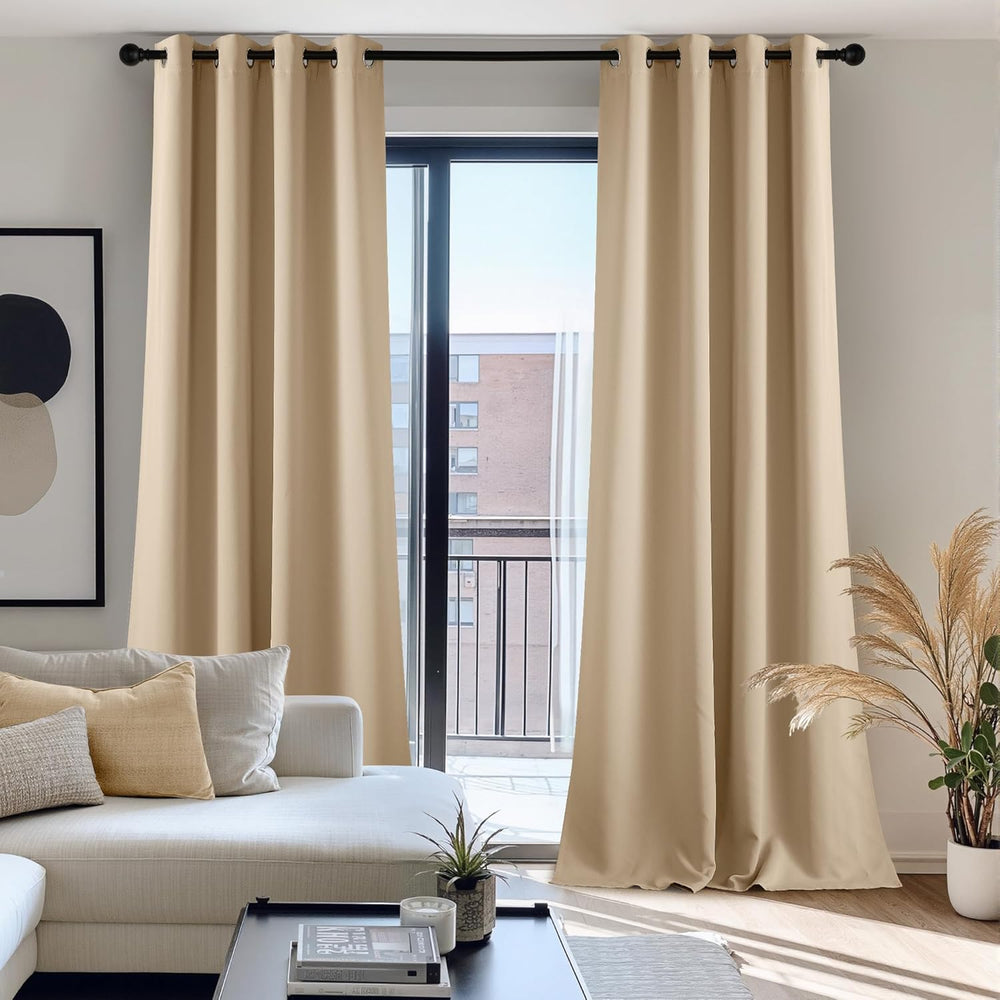 Pair of beige solid room darkening grommet top curtains hanging on a black rod in a modern living room.