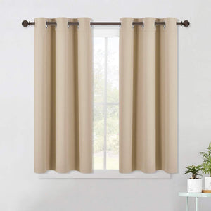 A pair of short beige blackout curtains with grommet tops hanging on a dark rod over a window.