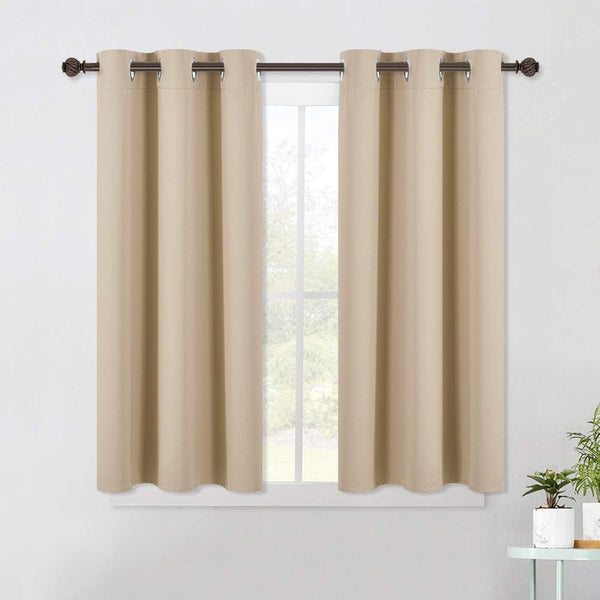 A pair of short beige blackout curtains with grommet tops hanging on a dark rod over a window.