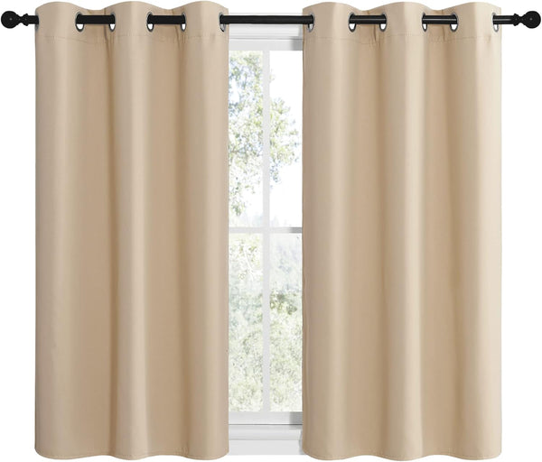 Two panels of smooth beige blackout curtains with metal grommets hanging on a black rod over a window.