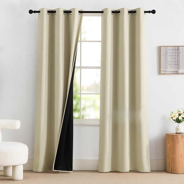 Beige grommet top blackout curtains with visible black lining hanging on a black rod in a bright room.