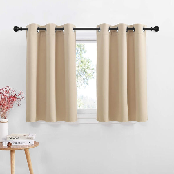 Two beige grommet top short window curtains hanging on a black rod, filtering sunlight.