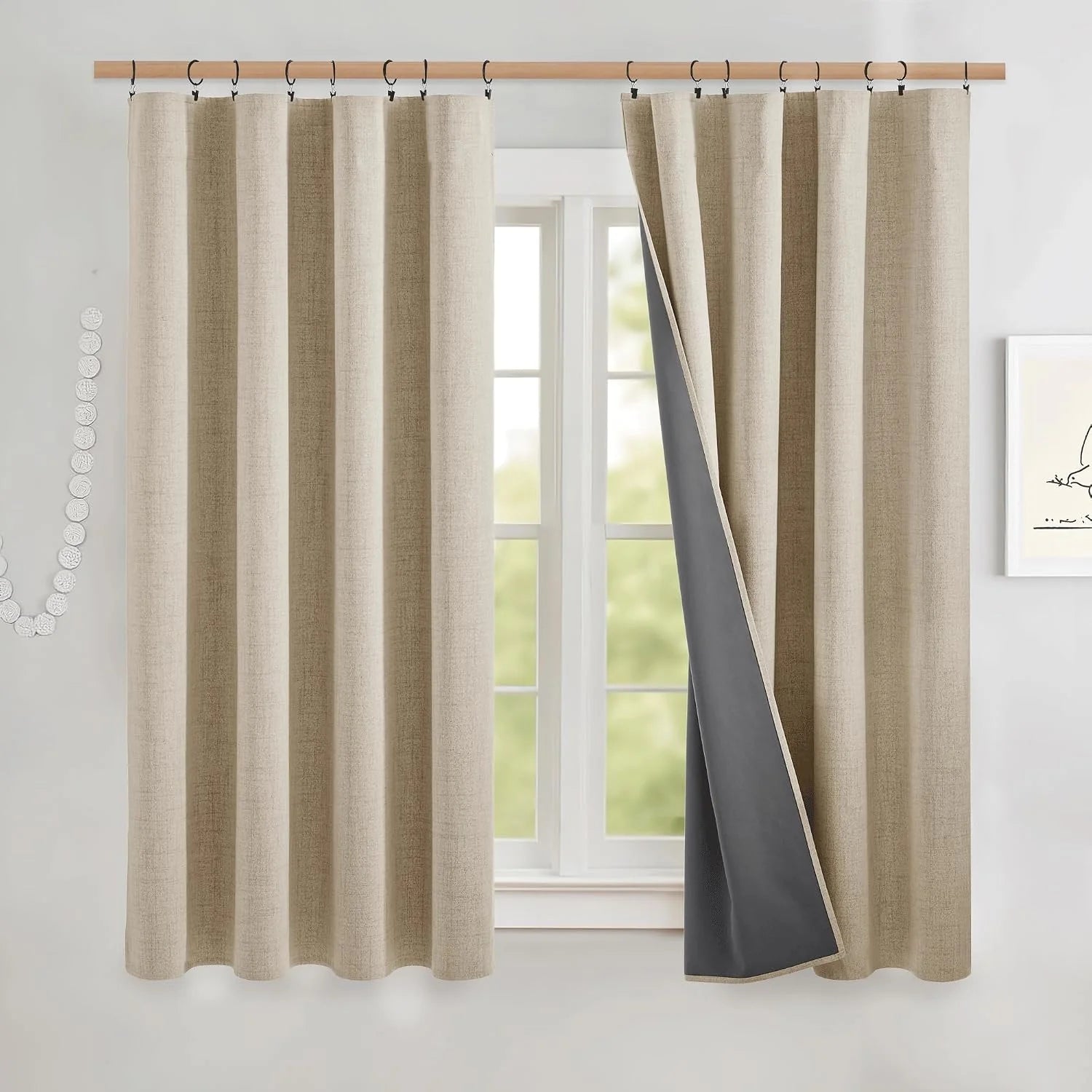 Beige linen-look blackout curtains with black ring hooks on a wood rod by a bright window