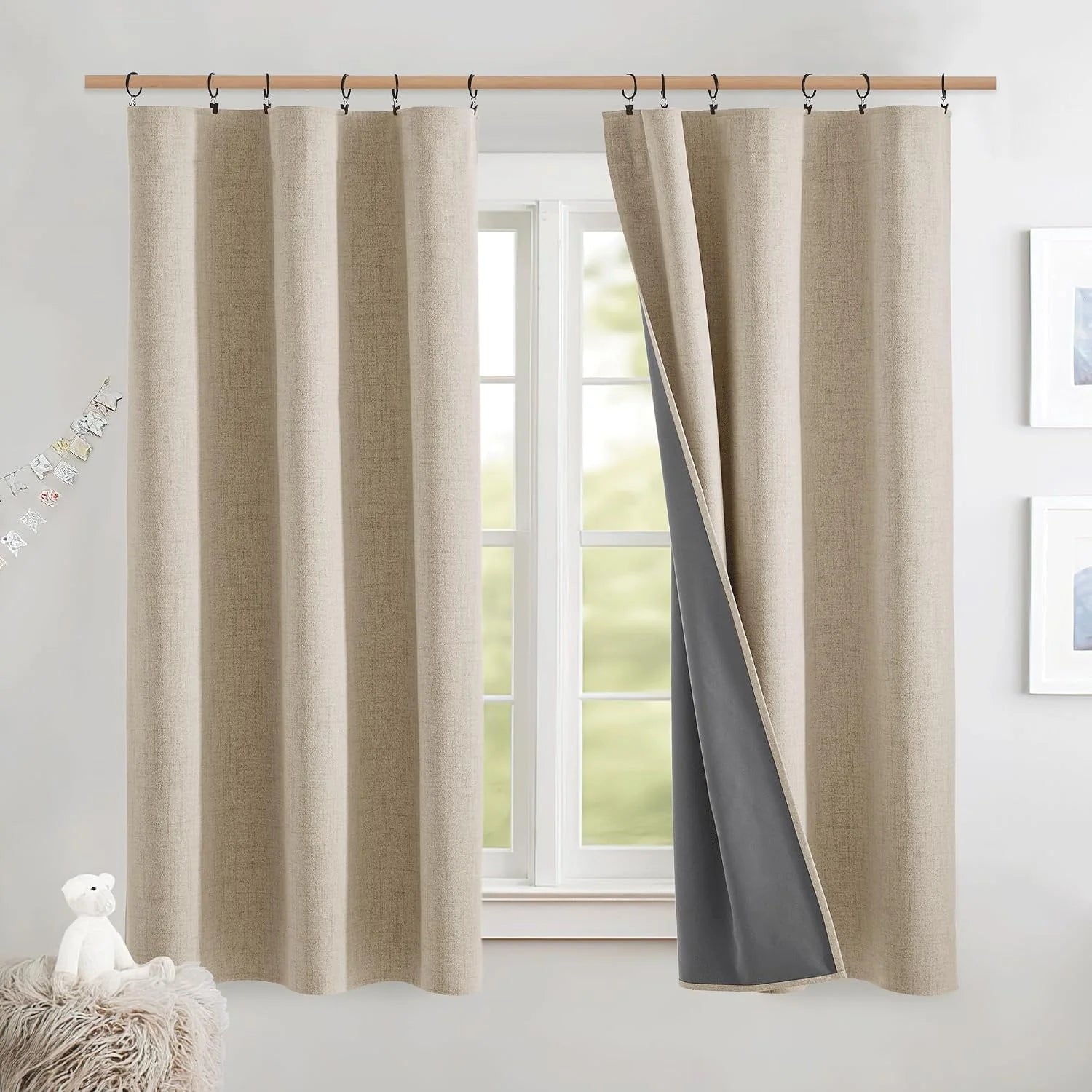 Beige textured blackout curtains with ring clips on a wooden rod in a bright nursery