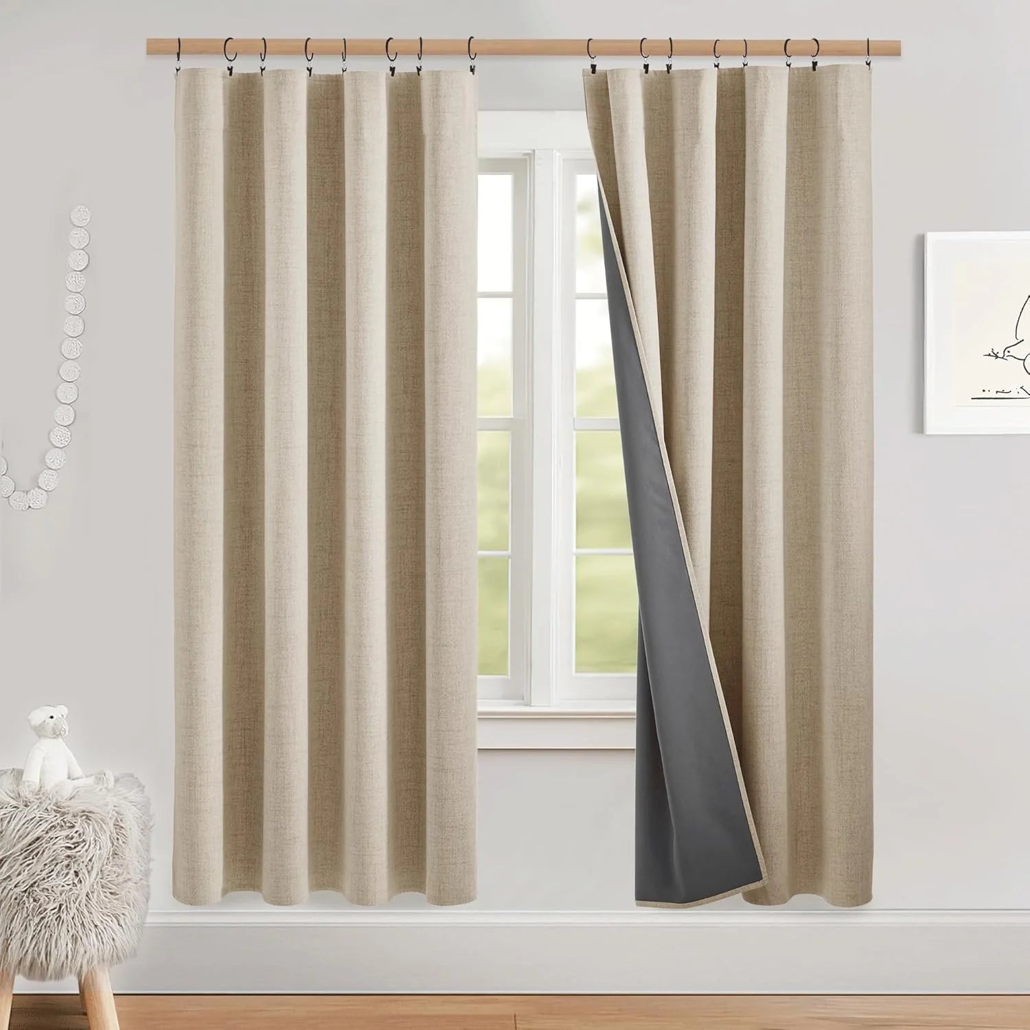 Beige linen-look blackout curtains with black liner on ring hooks in a bright nursery