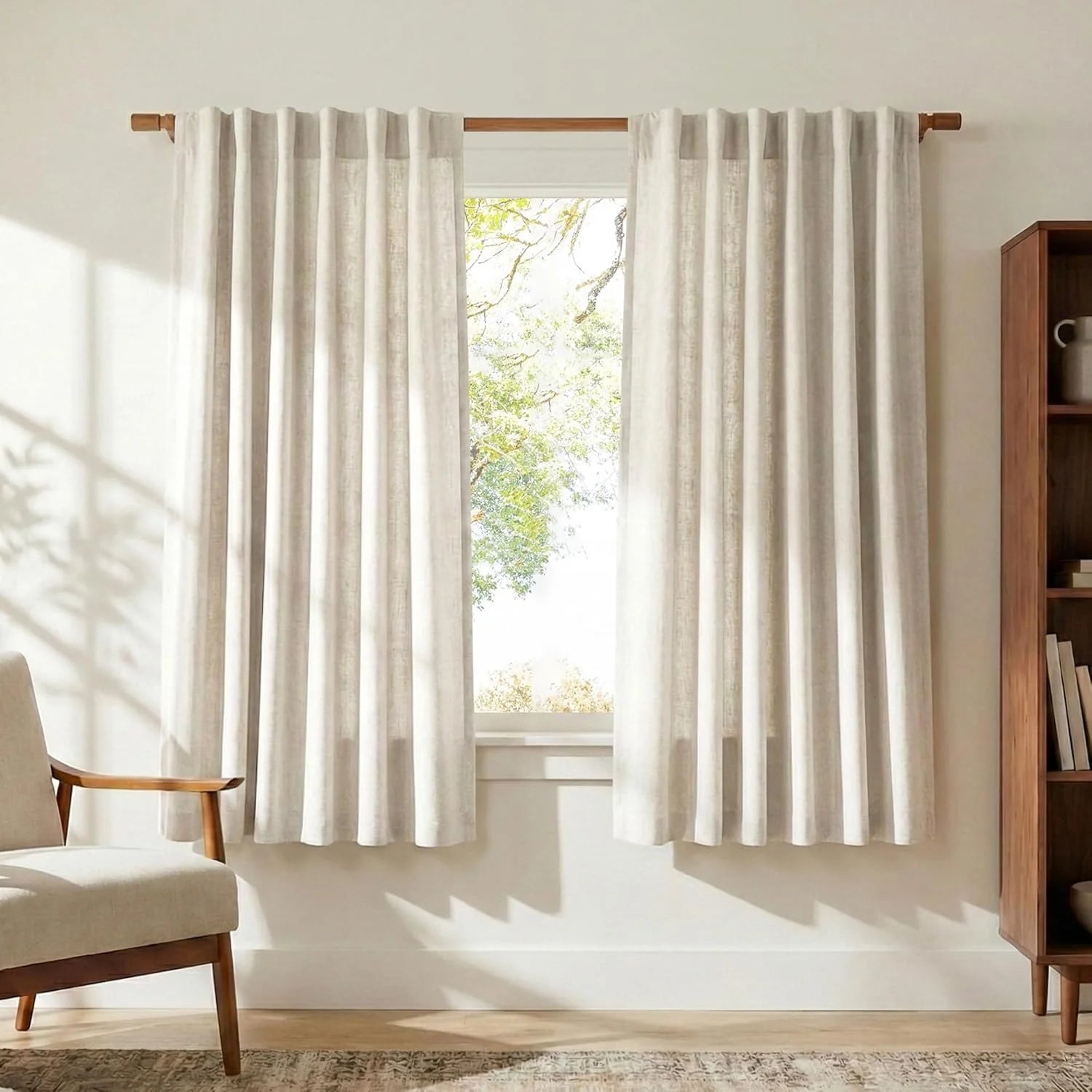 Beige linen curtains on a wooden rod in a bright, modern living room with an armchair