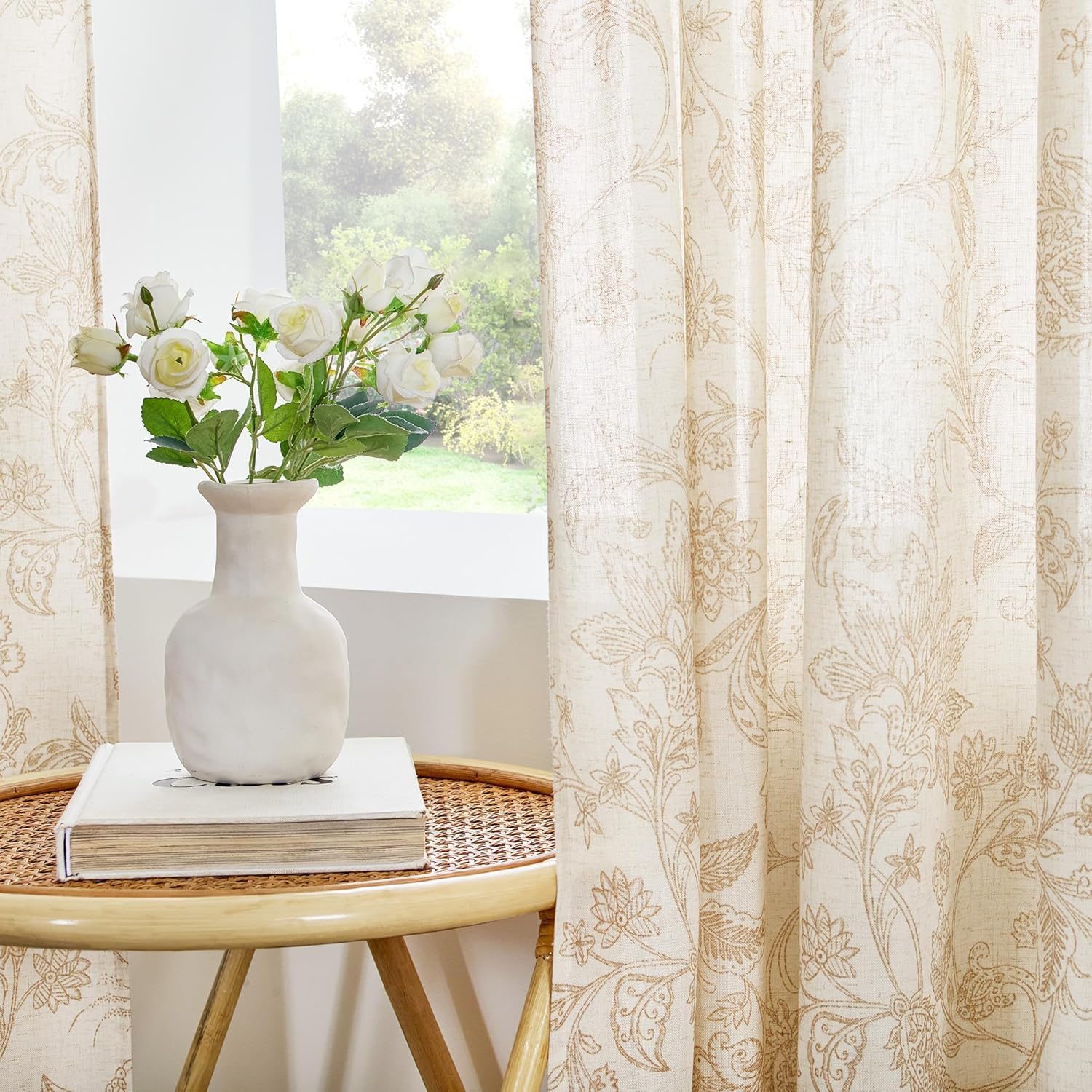 Light beige linen curtains with elegant tan floral embroidery filtering sunlight in a room.