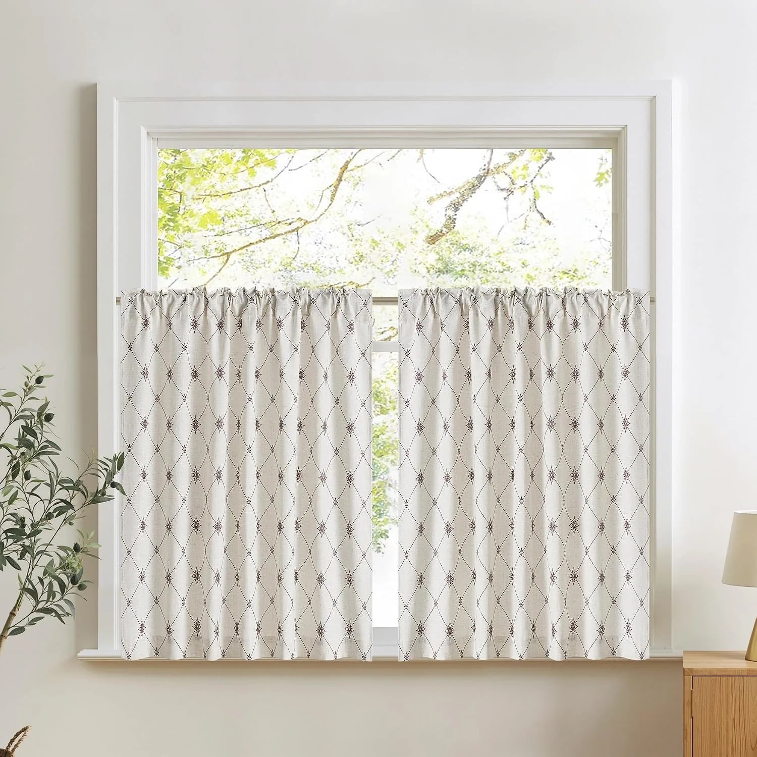 Beige linen cafe curtains with geometric embroidery on a bright white window