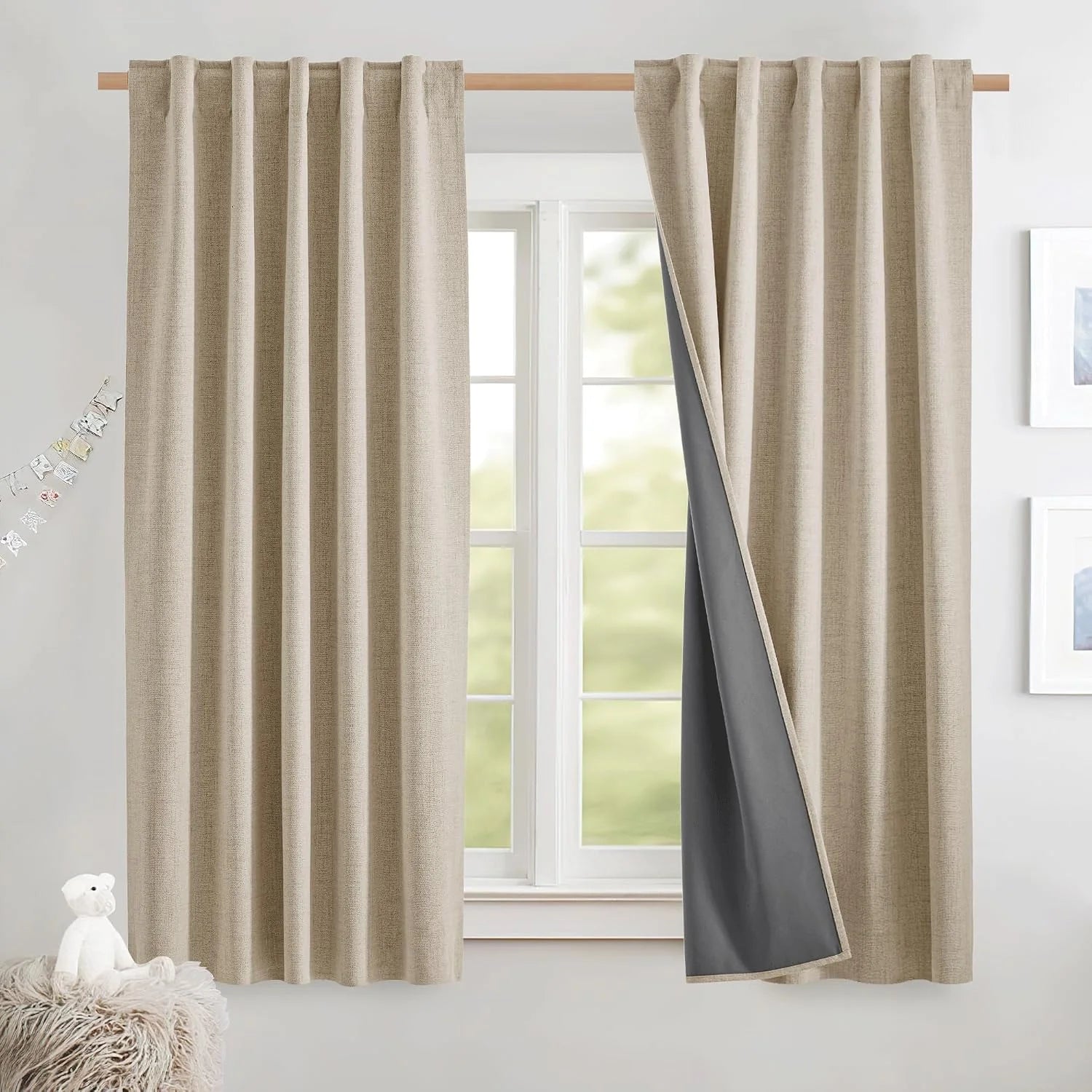 Beige linen-look blackout curtains on a wooden rod, one panel pulled back to show gray lining