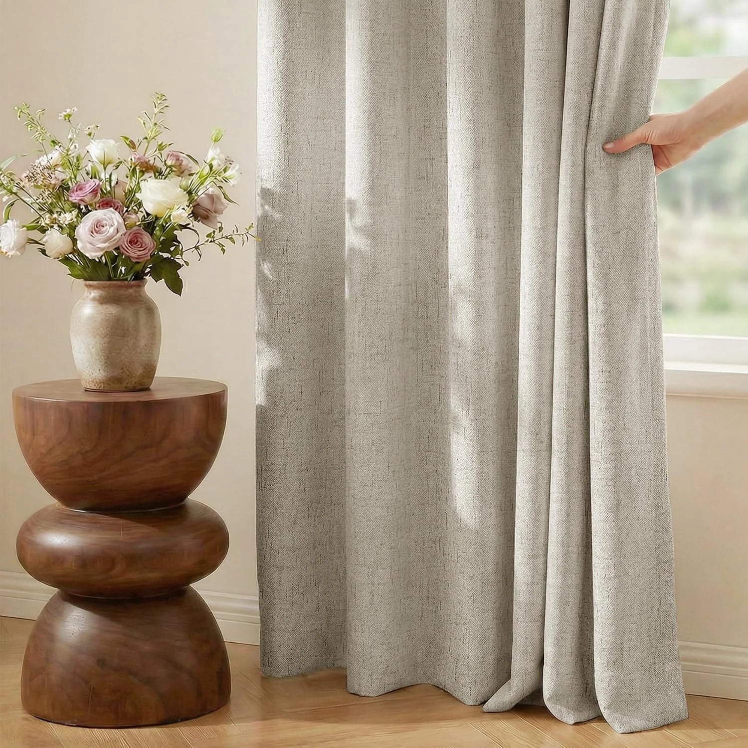 Beige linen-look curtain panel beside a window with a wooden side table and flowers