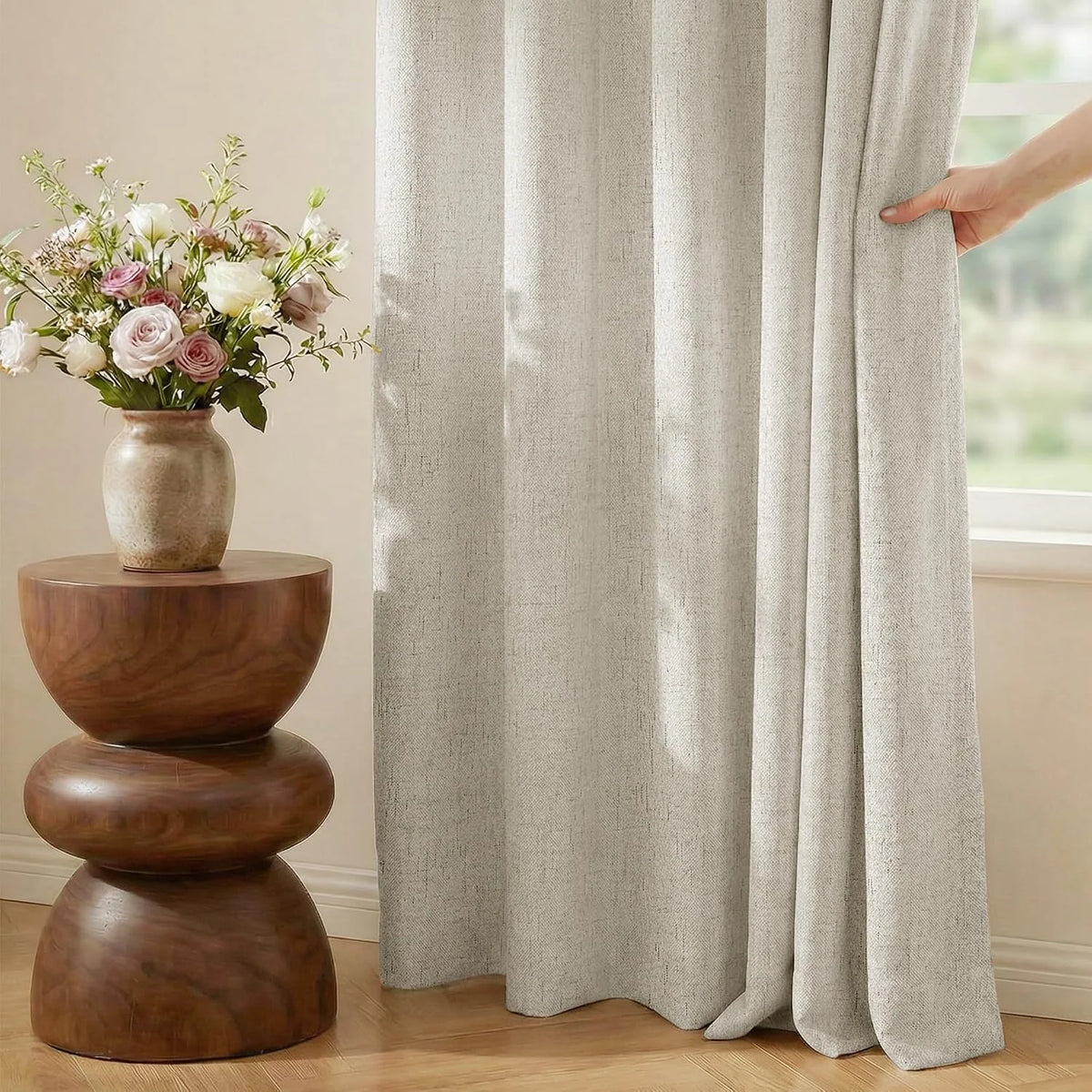 Beige linen-look curtain panel by a bright window beside a wooden side table and flowers