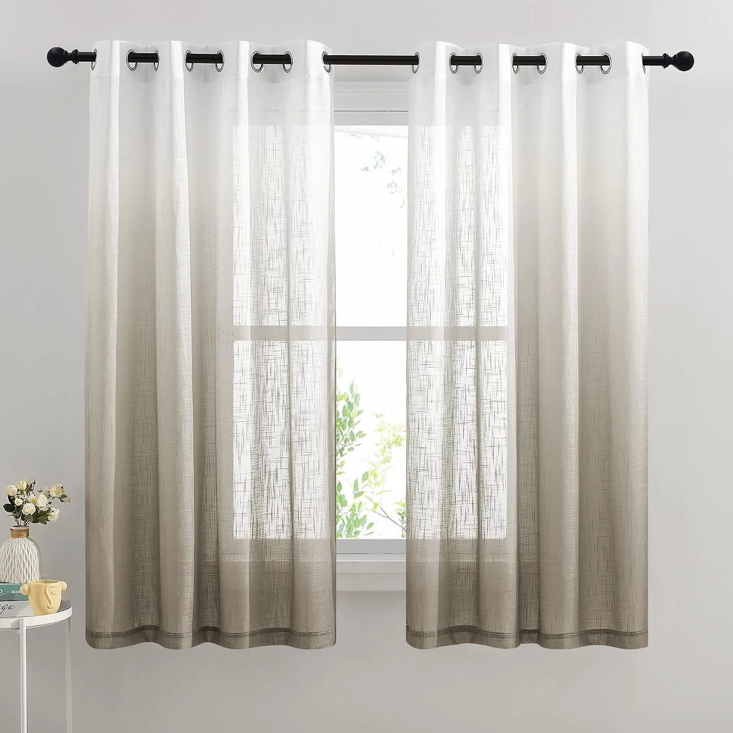 Beige sheer linen-look grommet curtains hanging on a black rod over a bright window