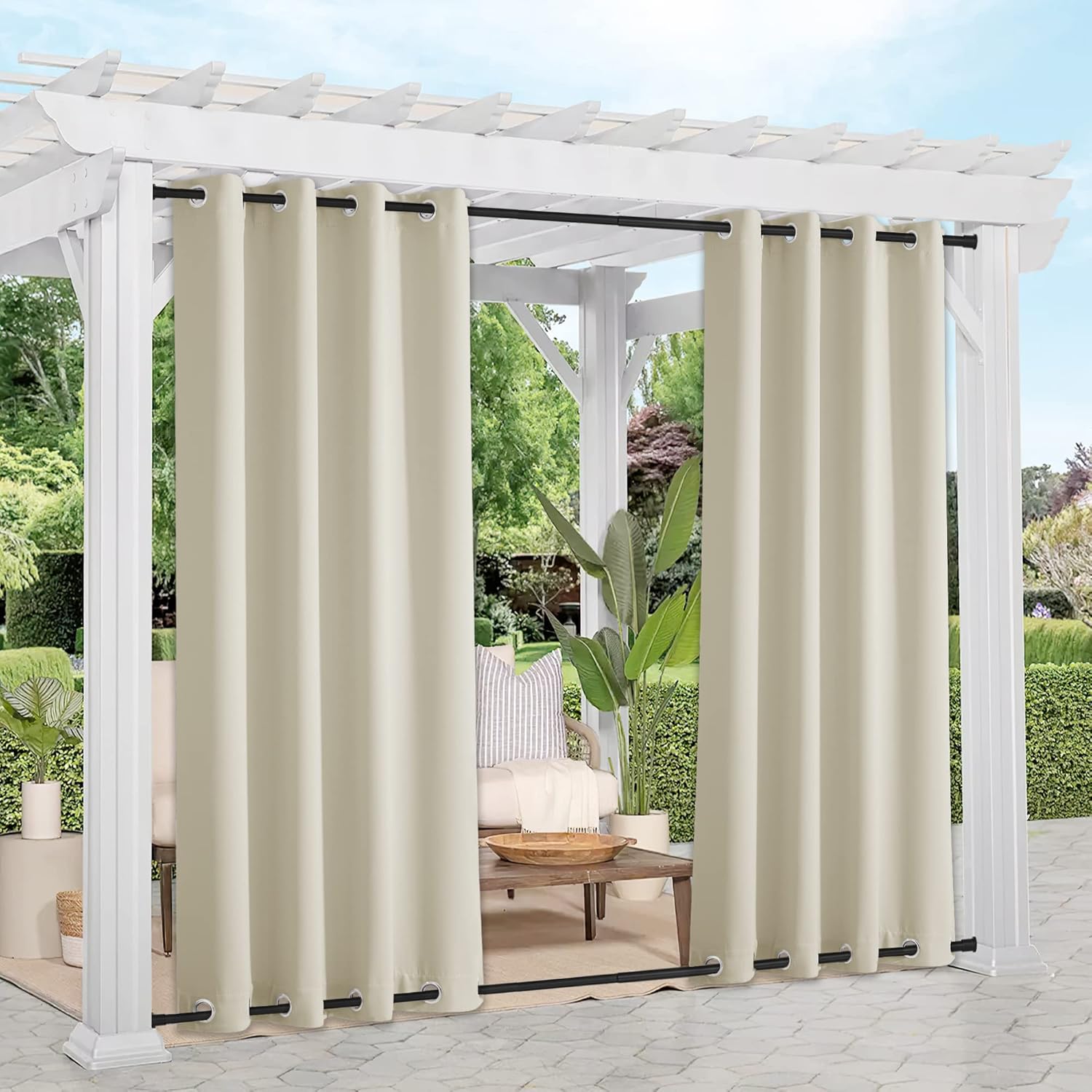 Beige outdoor patio curtains with black grommets hanging from a white pergola, offering privacy in a garden setting.