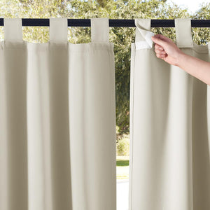 Beige outdoor tab top curtains with hook and loop fasteners. Hand adjusts tab on rod against green background.