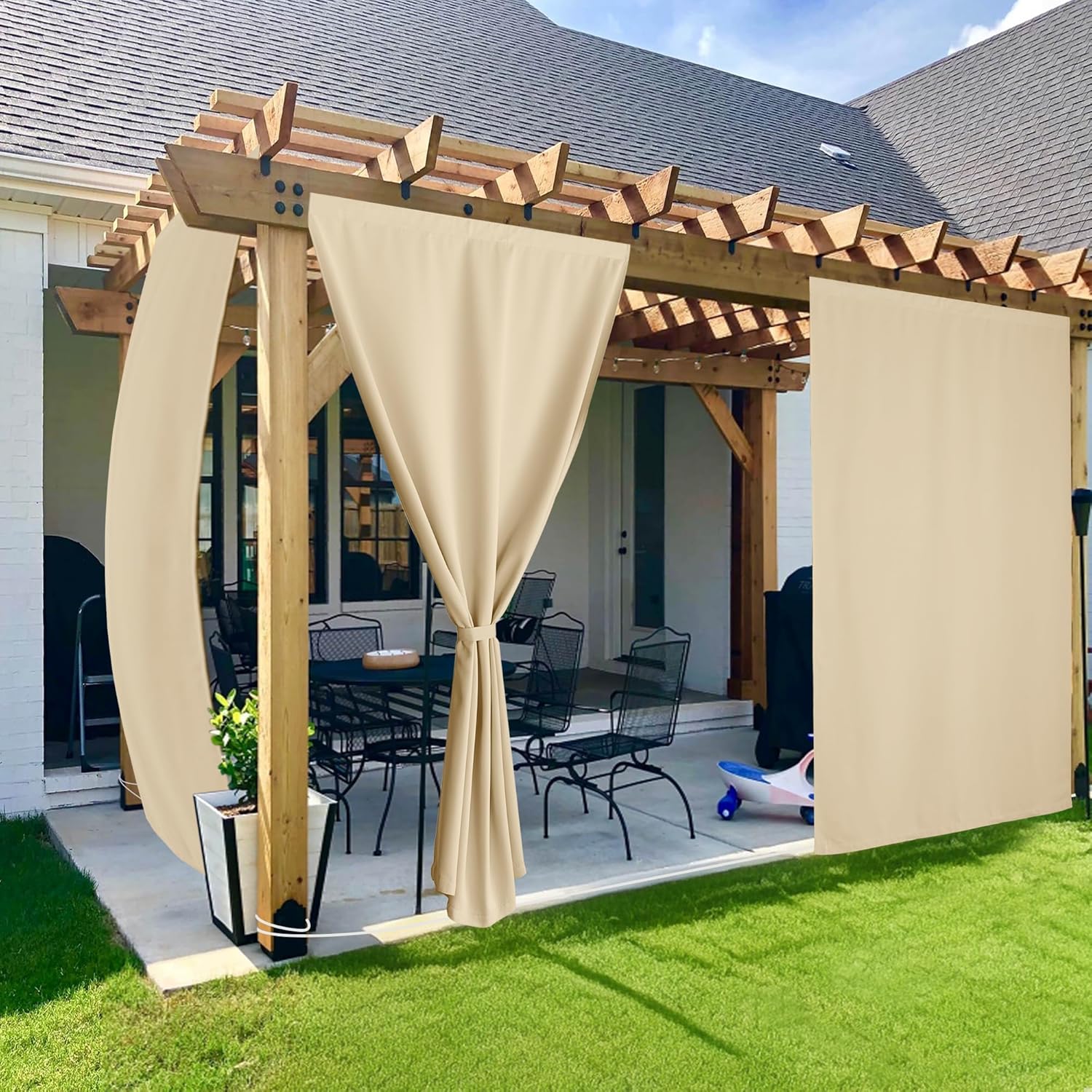 Beige outdoor patio curtains hanging from a wooden pergola, one panel tied back for shade and privacy.