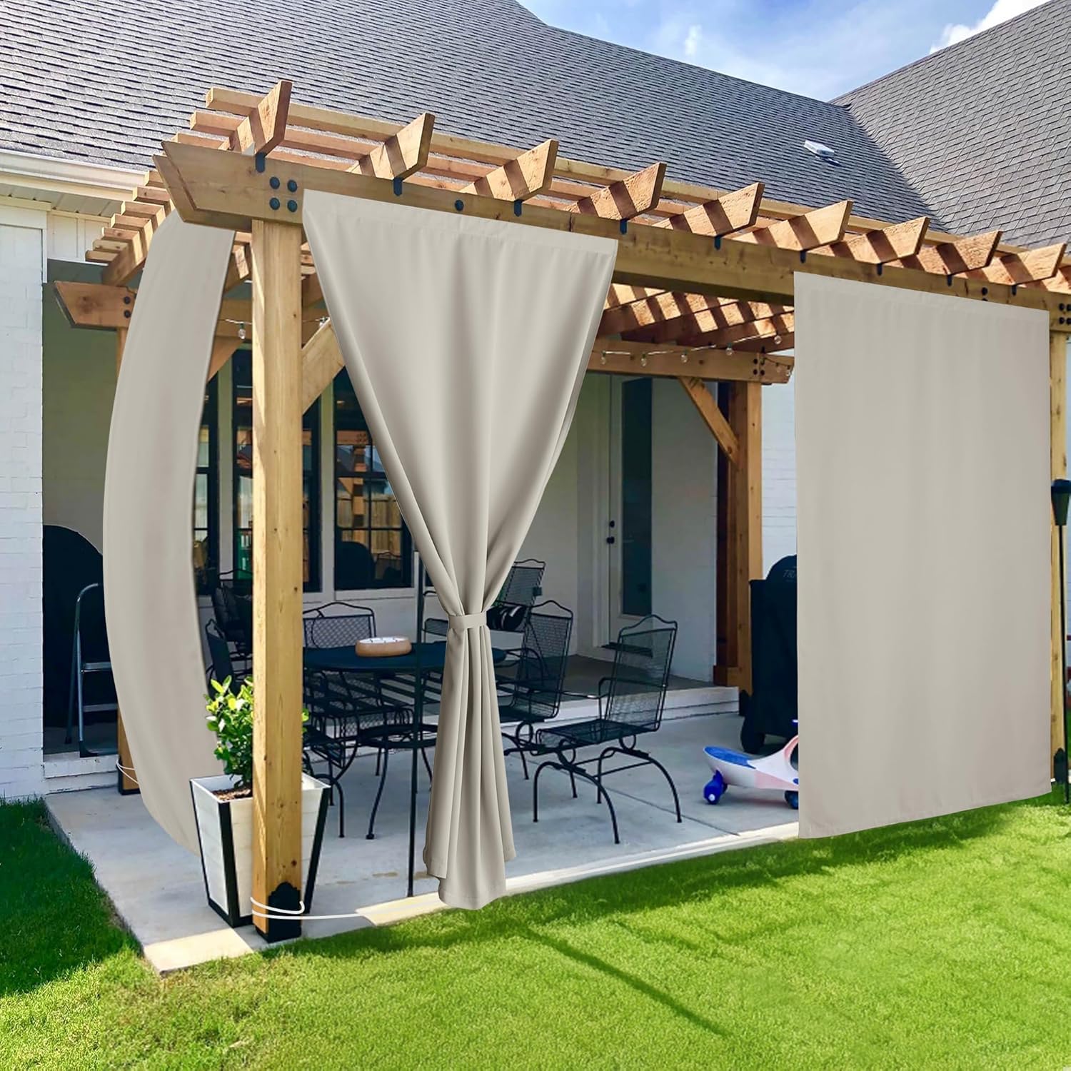 Beige outdoor curtains with grommet tops hanging from a wooden pergola on a patio, offering privacy and shade.