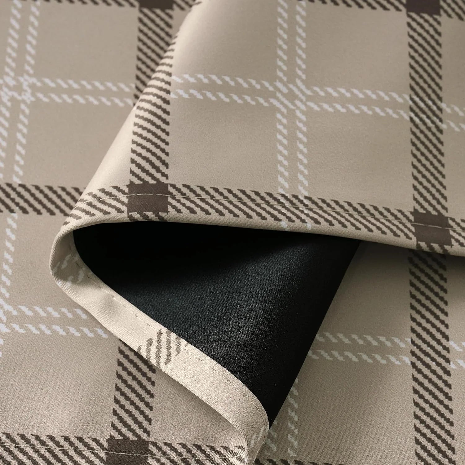 Beige plaid curtain fabric folded to show black blackout backing and stitched edge