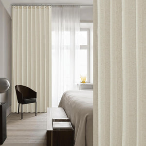 Textured beige linen pleated curtain panel on a silver rod, dividing a modern bedroom space.