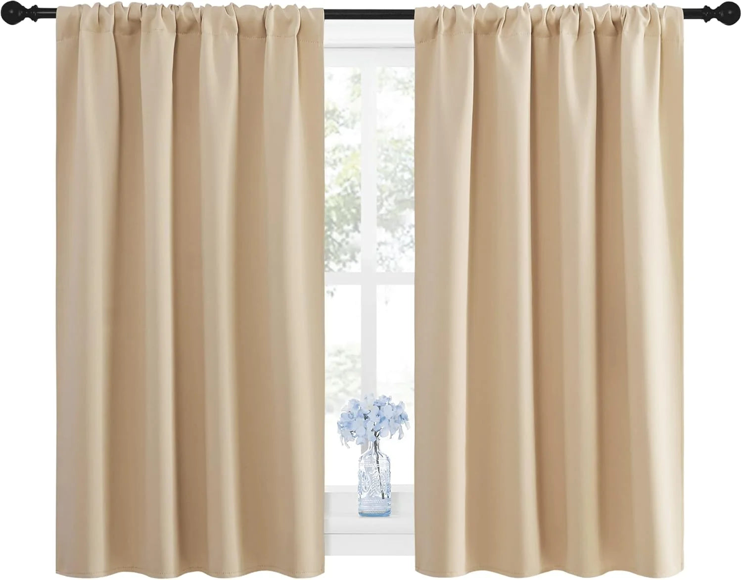 Beige rod pocket curtains in front of a bright window with a small blue floral arrangement.