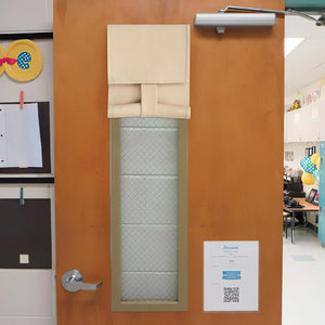 Beige roll-up door window cover attached to a wooden classroom door, providing privacy over a wired glass pane.