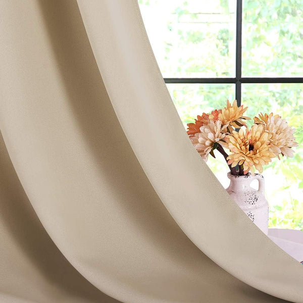 Smooth beige blackout curtain panel with gentle folds, partially covering window. Orange flowers visible.