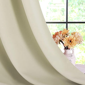 Close-up of a beige solid thermal blackout curtain panel draped next to a window with orange flowers.
