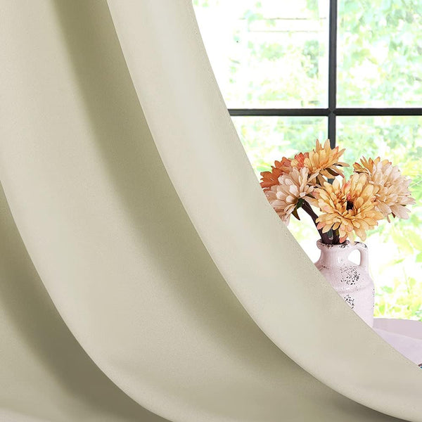 Close-up of a beige solid thermal blackout curtain panel draped next to a window with orange flowers.