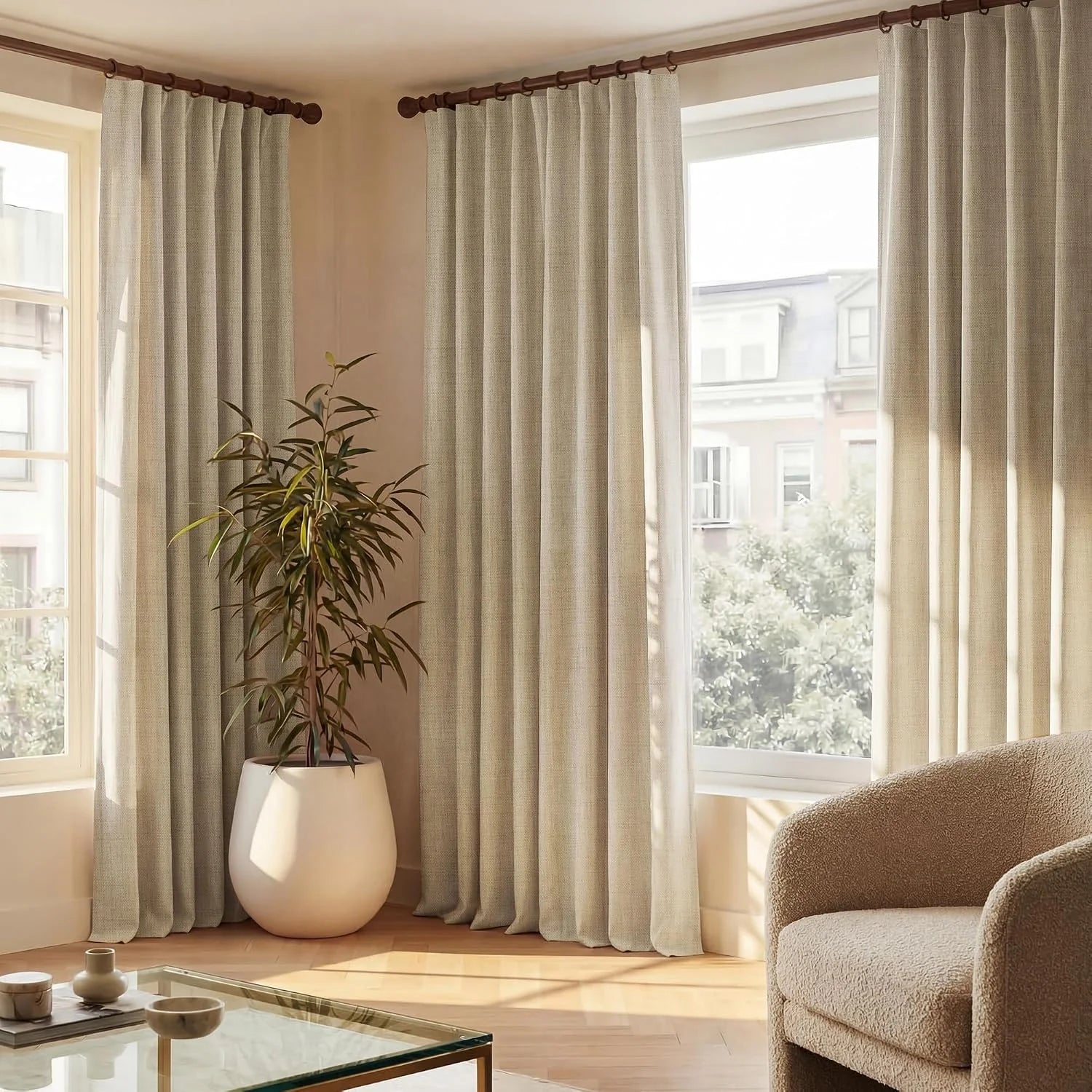 Light beige textured drapes on wooden rods in a modern living room with a plant and natural light.