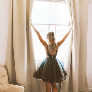 Beige textured room darkening curtain panels pulled open by a woman, revealing bright window light.
