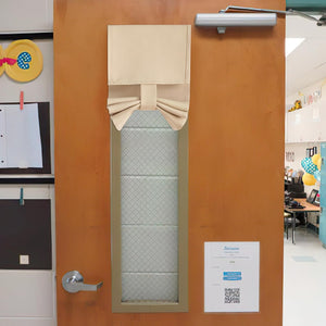 Beige fabric tie-up door window shade covering the upper portion of a classroom door window for privacy.