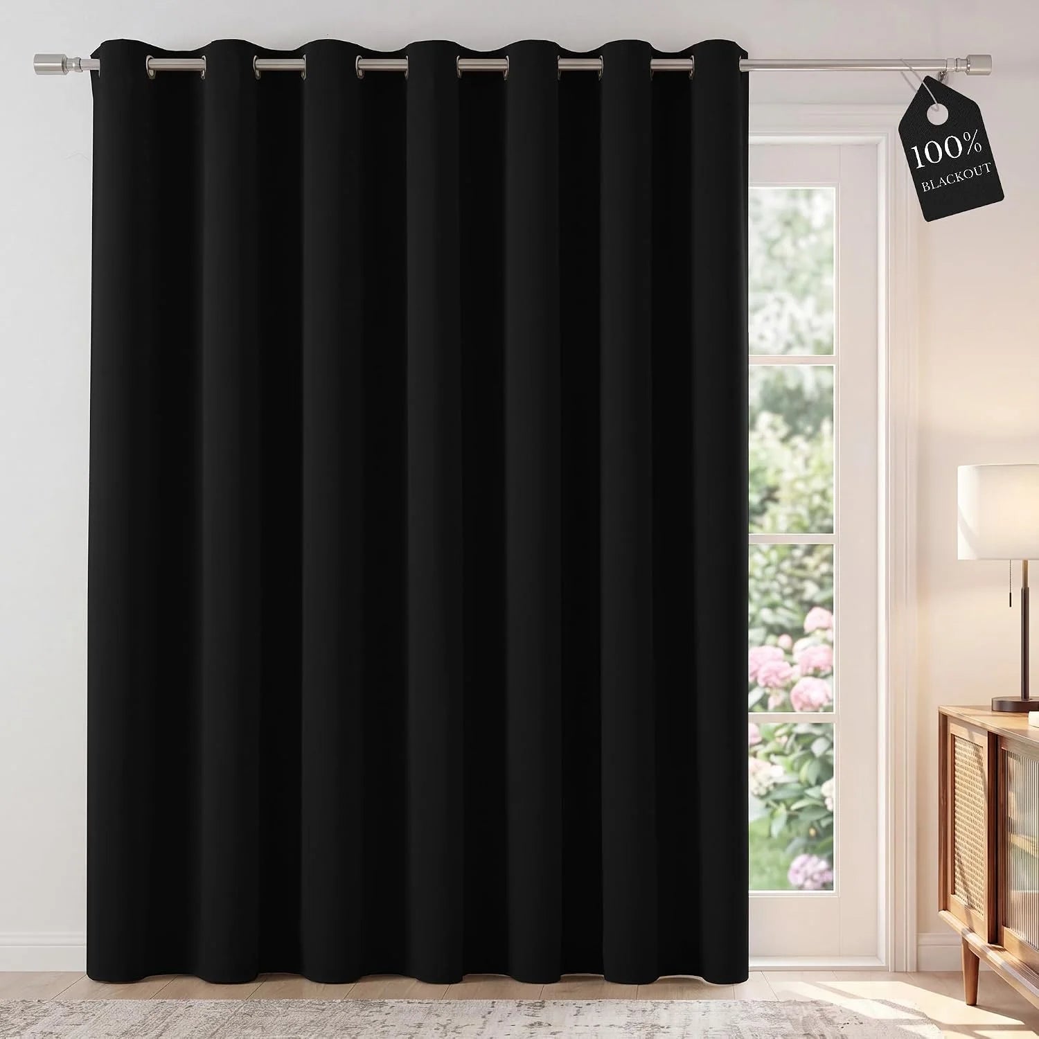 Single black blackout curtain panel with silver grommets over a patio door