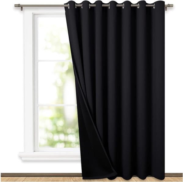 Black grommet top blackout curtain panel hanging on a window rod, partially open.
