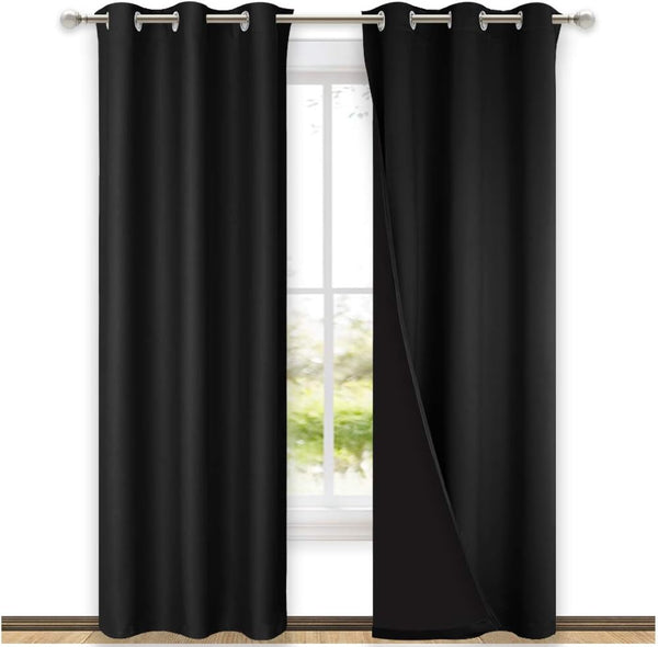 Black blackout grommet curtains hanging on a rod over a window. One panel is open, showing the thick fabric.