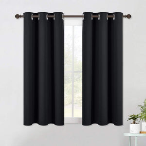 Pair of solid black blackout curtains with silver grommet rings on a bronze rod over a sunlit window.