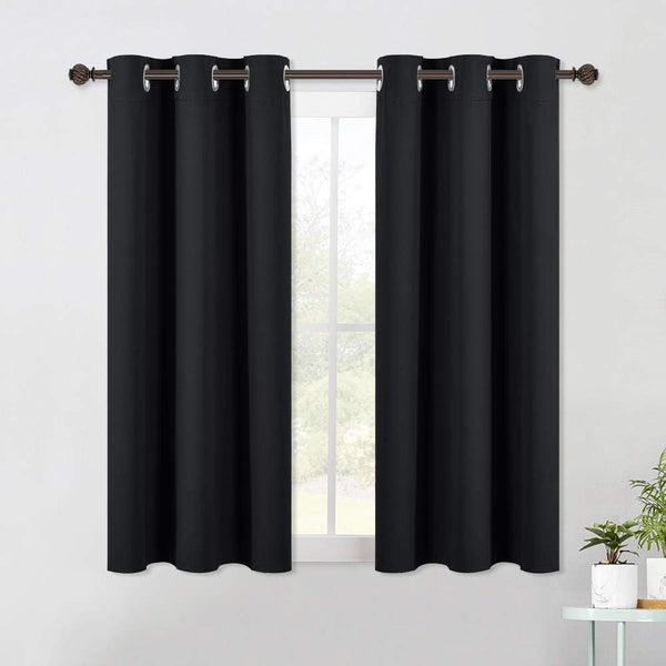 Pair of solid black blackout curtains with silver grommet rings on a bronze rod over a sunlit window.